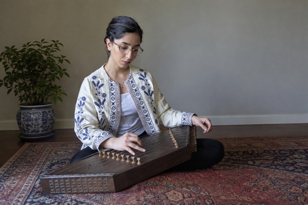 Niloofar sits with a santur on a persian carpet