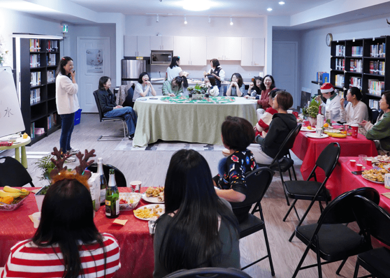 People congregate in a room around tables with a speaker at the front of the room.
