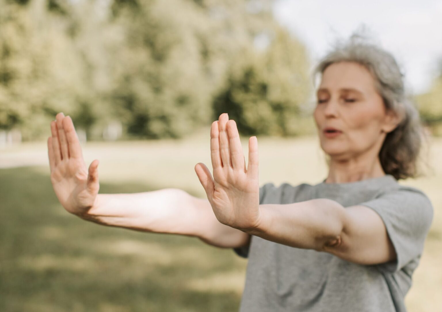 A woman with her eyes closed stretches her arms outdoors