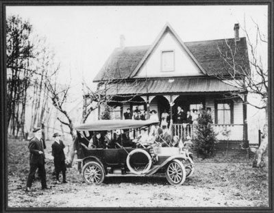 A black and white photo of the Navvy Jack house with a car and some people infront of it. 