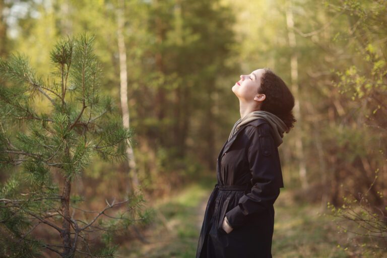 A woman leans her head back and breaths in contentment in a sunlit forest.
