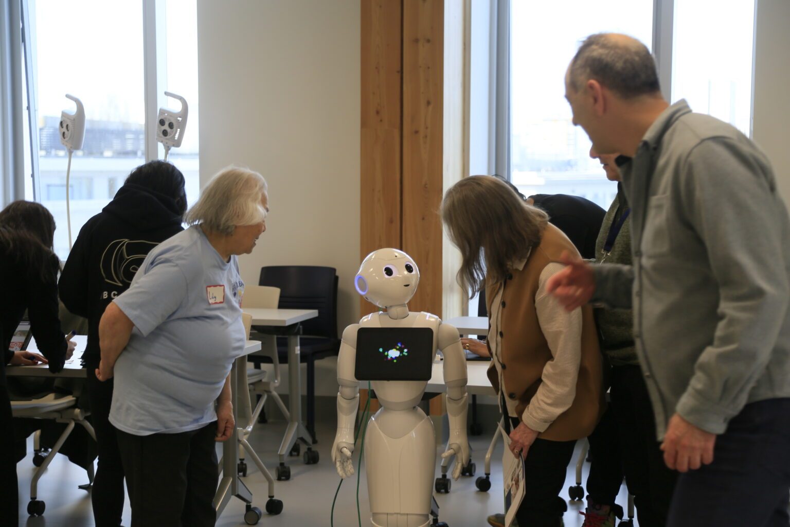 Elders gather around to  look at small robot with a screen on its chest 