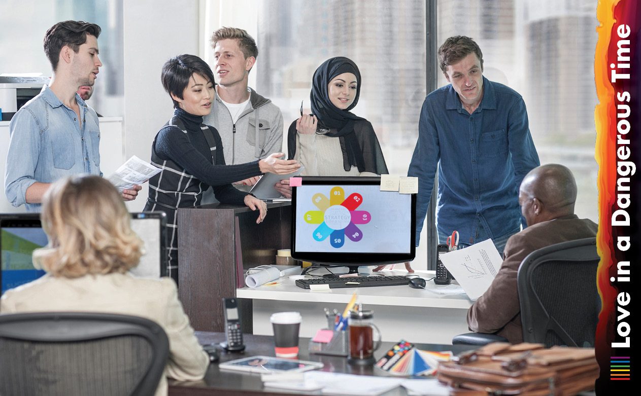 A diverse group of employees gather around a computer, looking at the screen. 