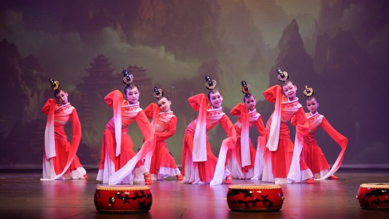 Seven individuals dressed in traditional red dancewear performing a Chinese dance on stage.
