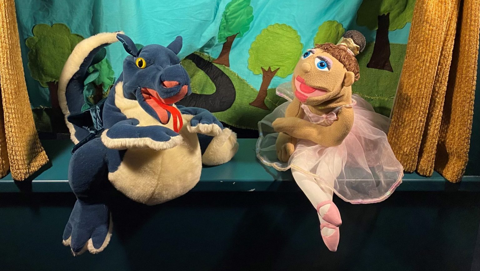 A dragon and a ballerina puppet perch on the side of the puppet show stage.